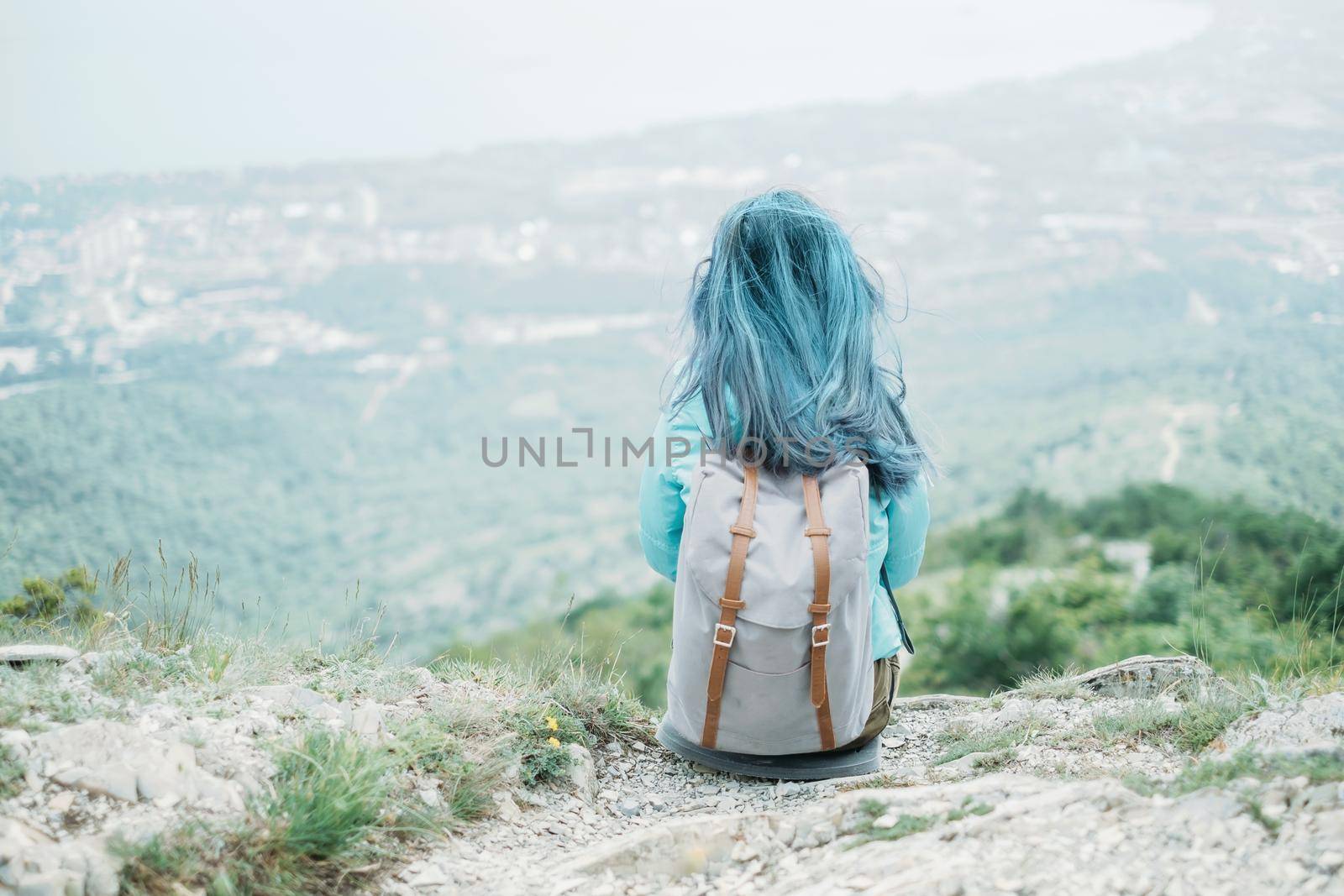 Traveler young woman with backpack resting on peak of mountain, rear view