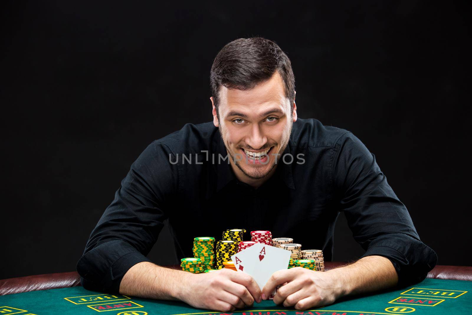 Happy poker player winning and holding a pair of aces sitting at a poker table with chips