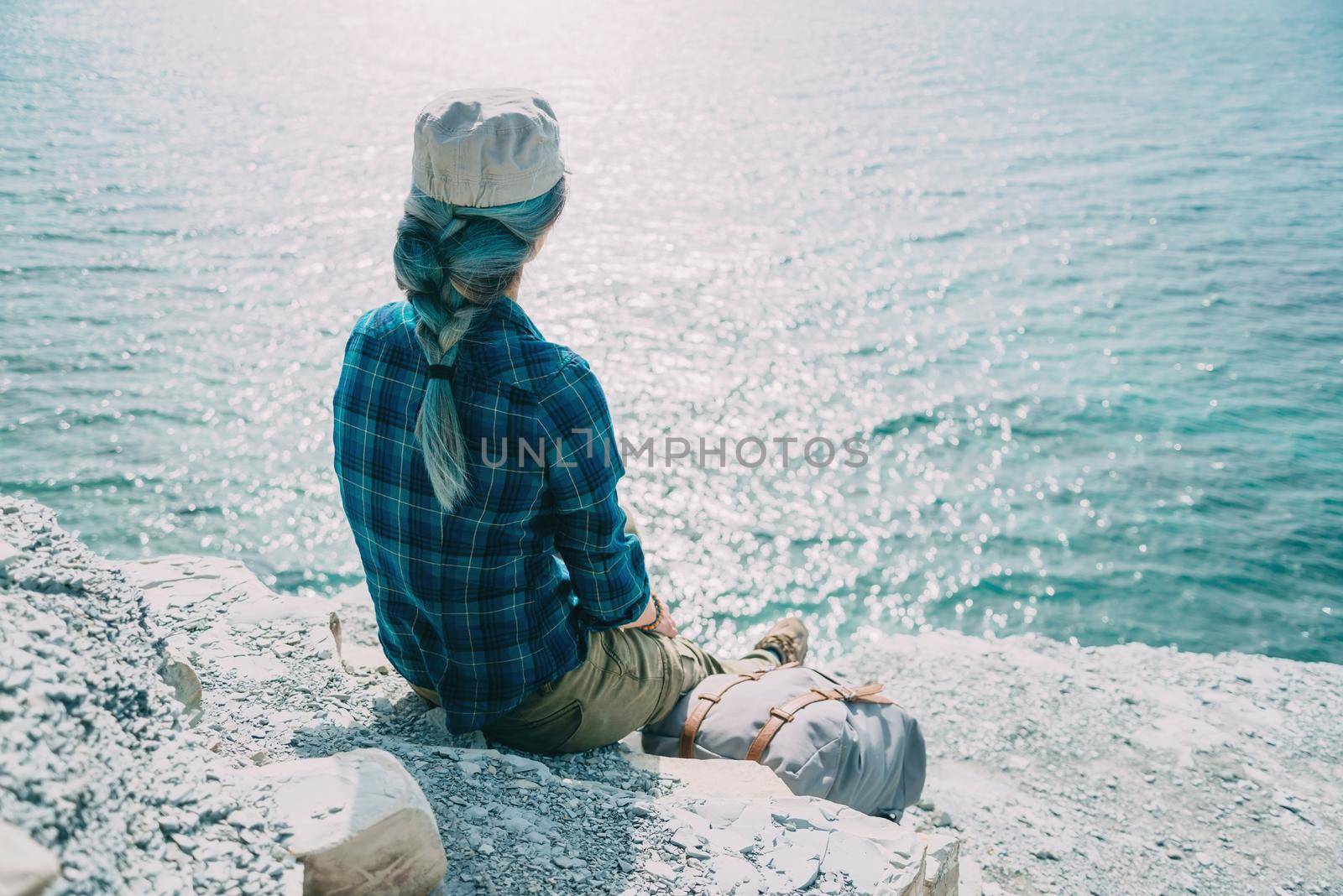 Traveler young woman sitting on steep coast and enjoying view of sea, rear view