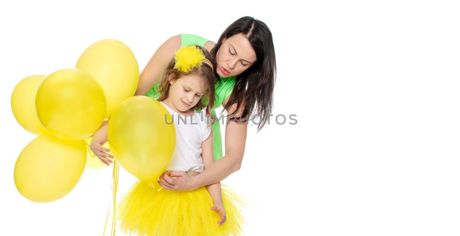Beautiful young mother in a short green dress and her little beloved daughter , with yellow balloons in her birthday.Isolated on white background.