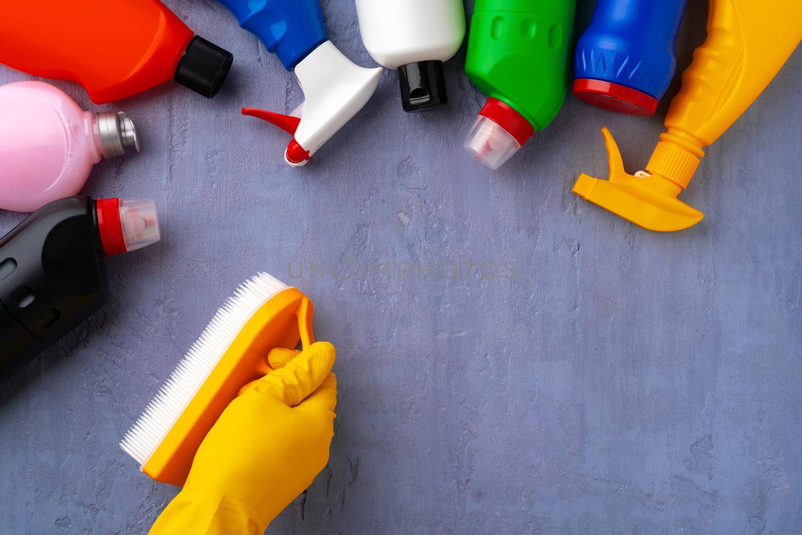 Cleaning supplies with hands in rubber gloves on gray background, top view