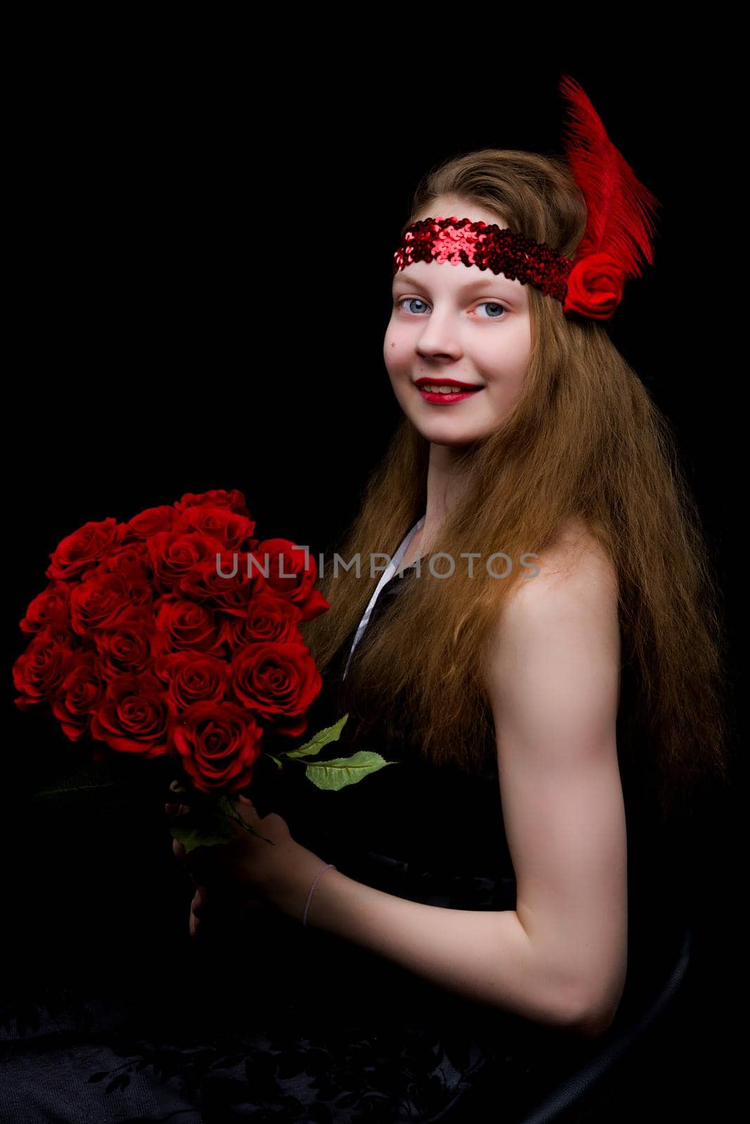 A beautiful teenage school girl is photographed in the studio with a large bouquet of flowers, against a black background.