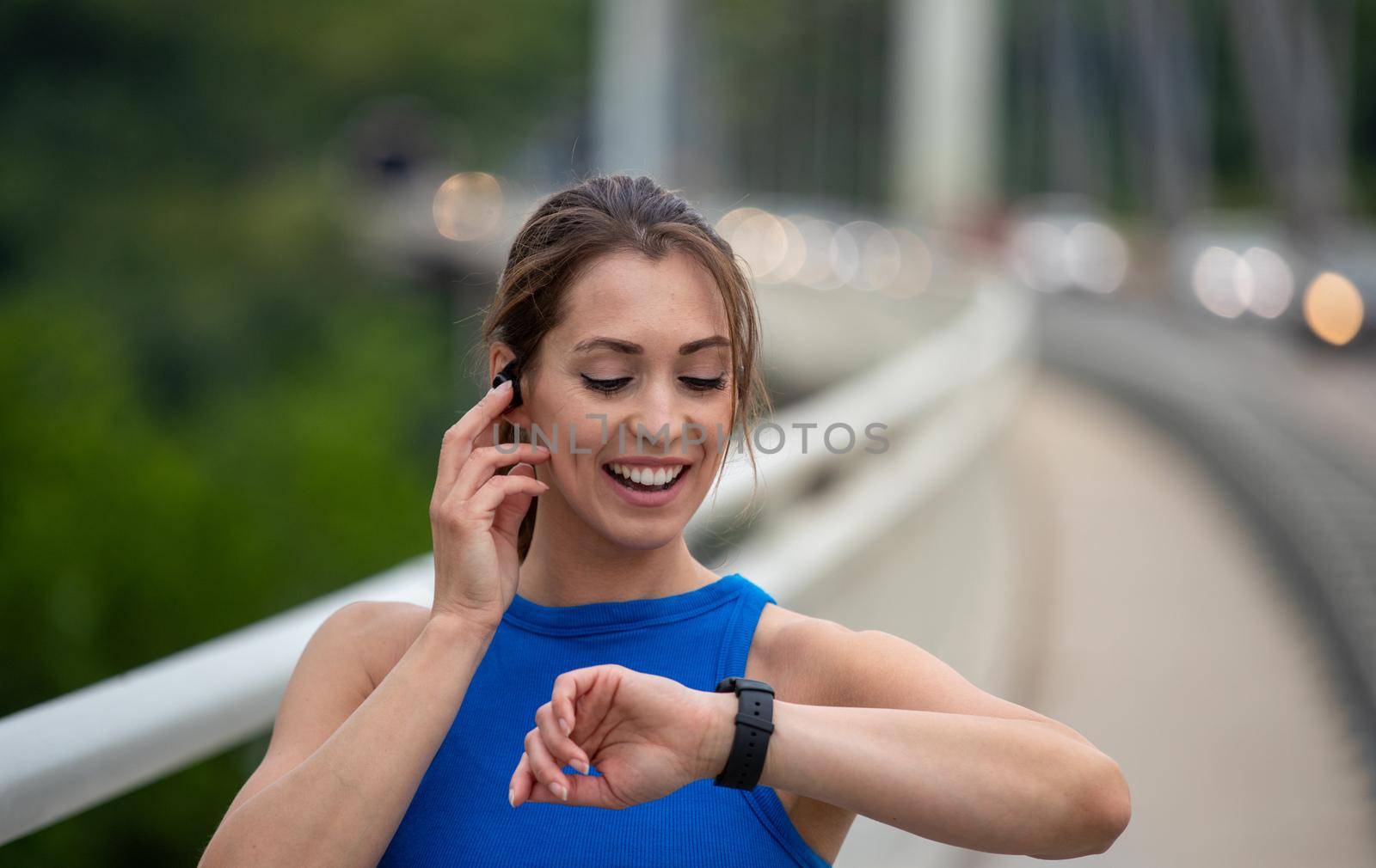 Young athlete exercising outdoors on bridge. Runner using smart watch for health data and statistics.