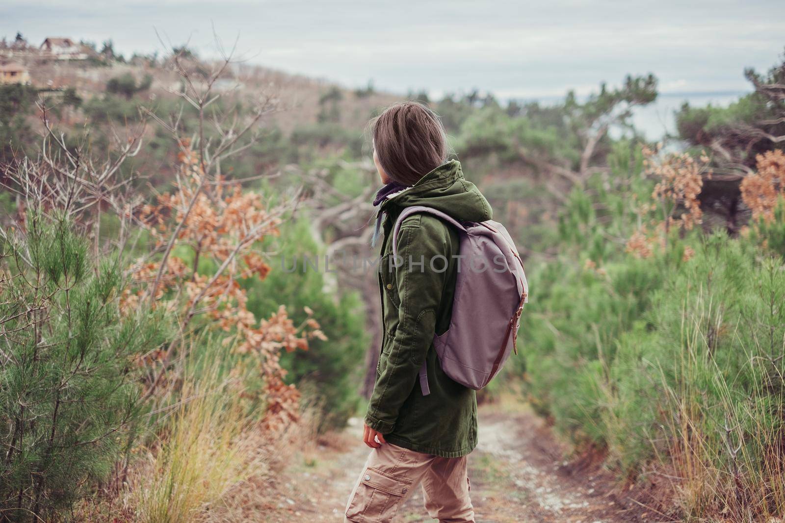 Hiker girl wearing in parka jacket and cargo pants with backpack standing on footpath in the forest