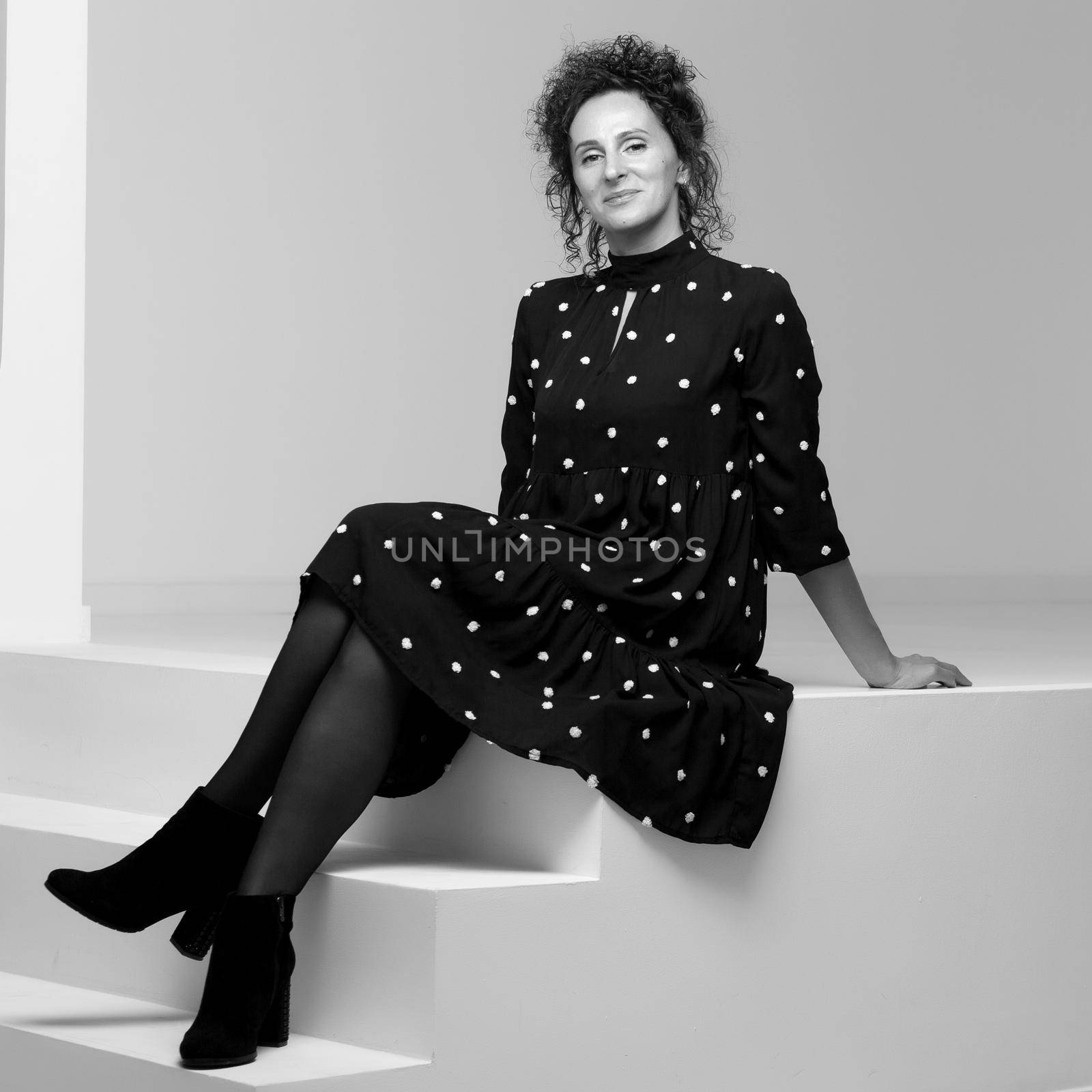 A beautiful young woman is sitting in a studio on a white staircase. Style and fashion concept.