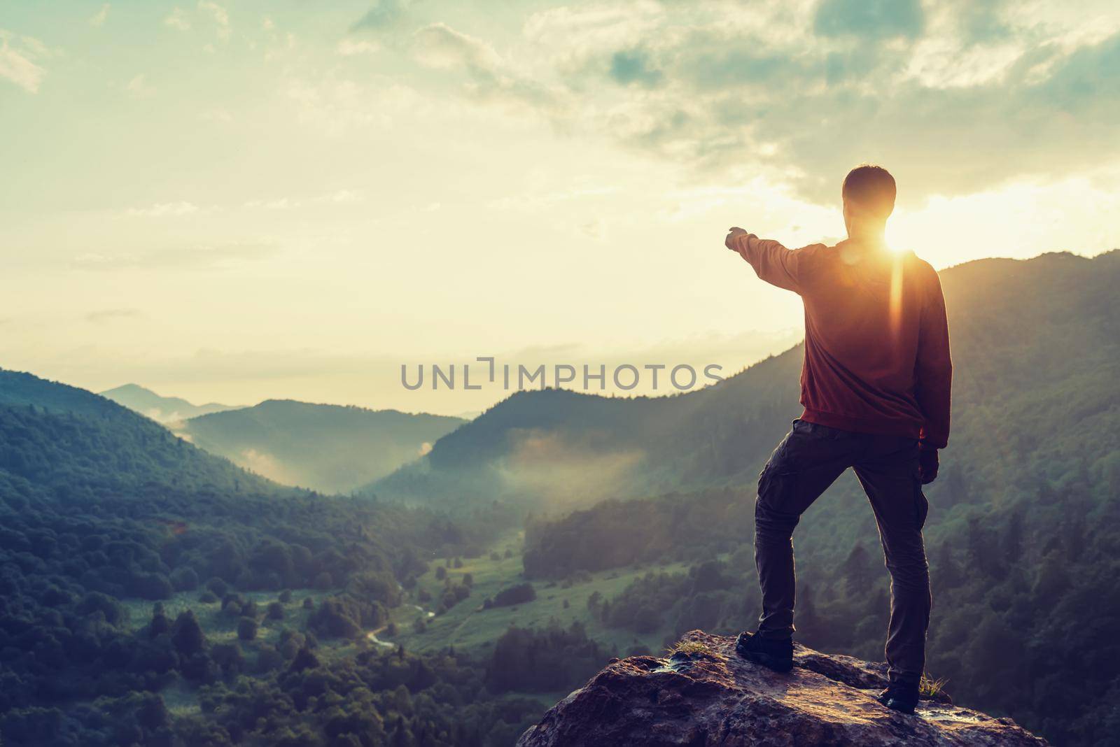 Young man pointing at something in the distance in summer mountains at sunset. Toned image