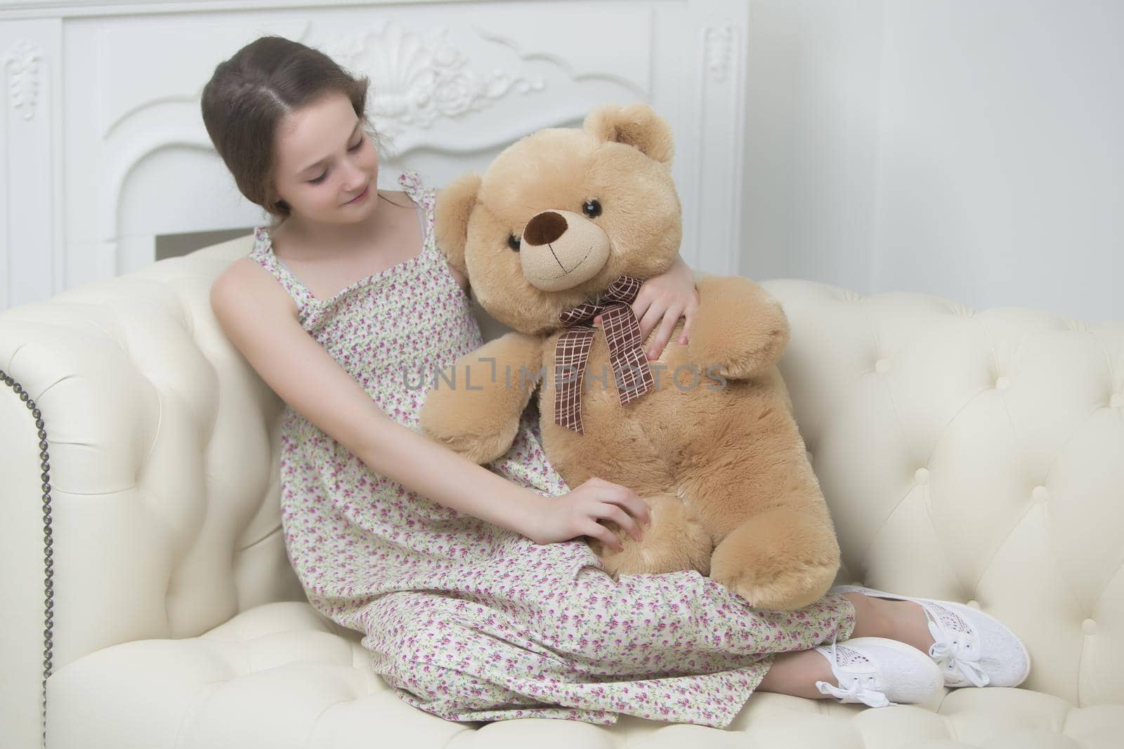 A teenage girl of school age is sitting on the couch with a big teddy bear. The concept of a happy childhood.