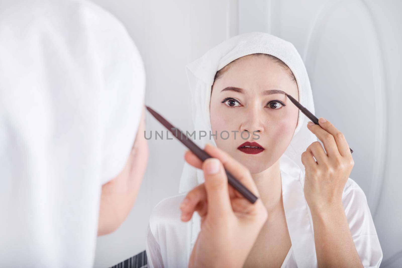 Beautiful woman looking mirror and using pencil makeup eyebrow 