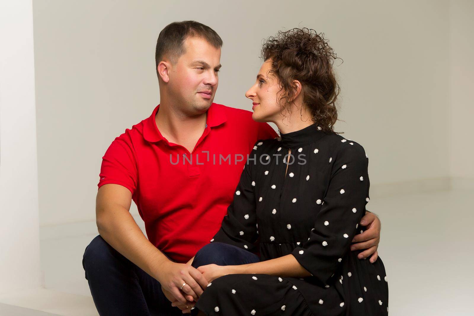 Beautiful family man and woman are sitting on the white stairs in the studio. The concept of love, friendship.