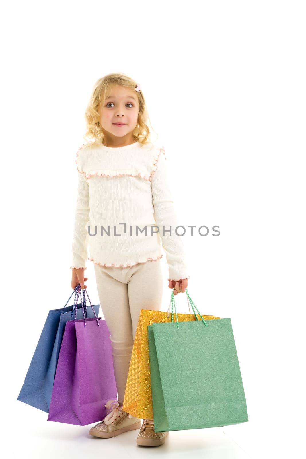 A cheerful little girl is shopping in a store with large, multi-colored paper bags. The concept of holidays, advertising sales. Isolated on white background.