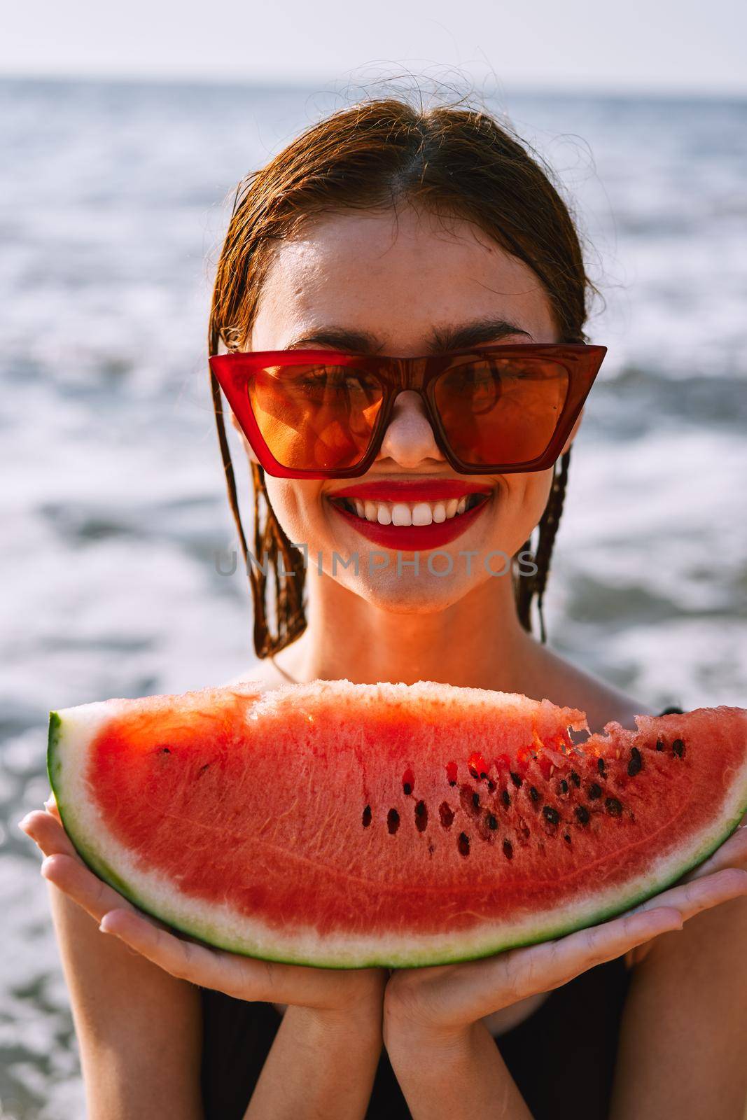 cheerful woman in sunglasses eating watermelon by the ocean. High quality photo