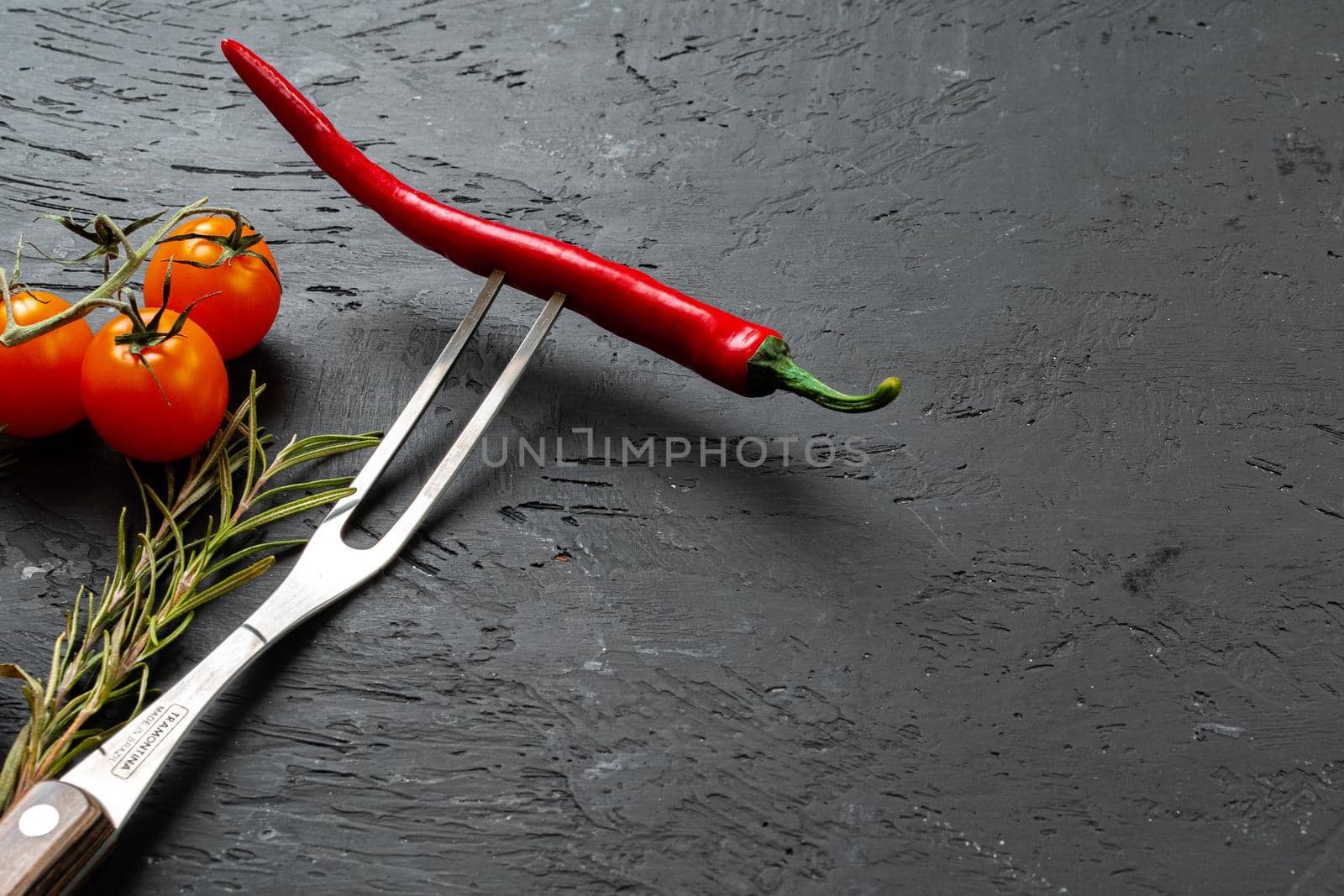 Red chili pepper on fork on black stone background close up