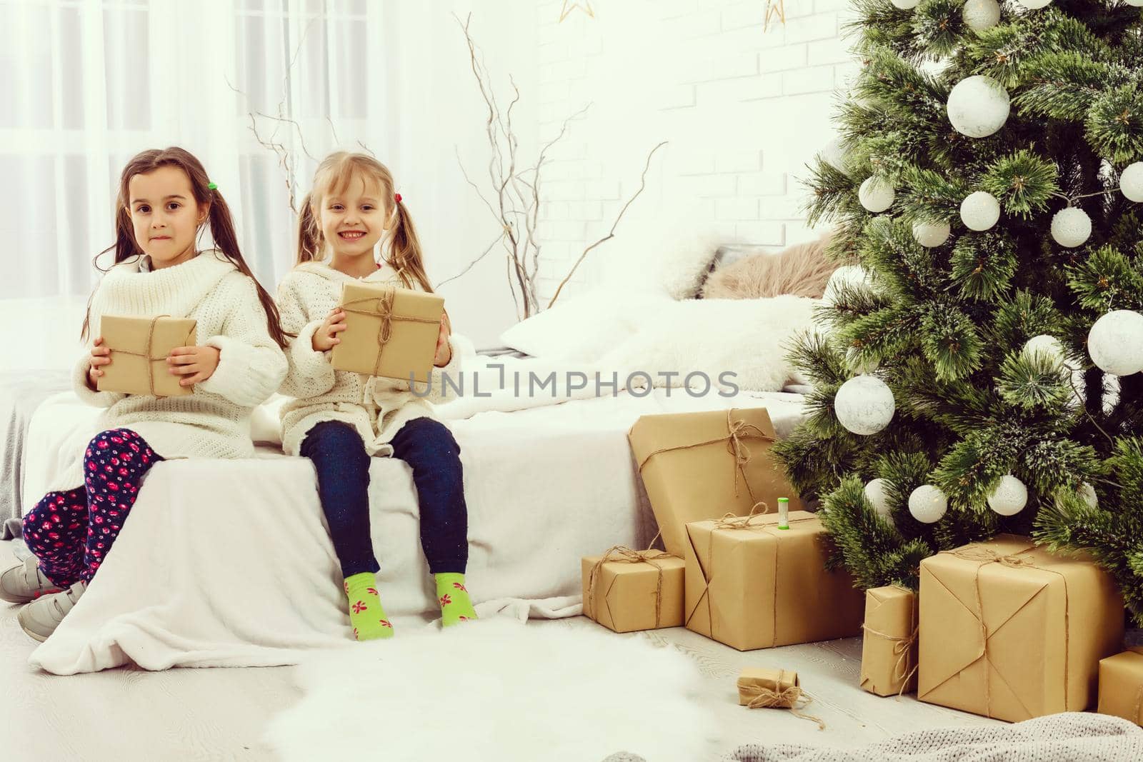 two girls in front of christmas tree with gifts and fire place