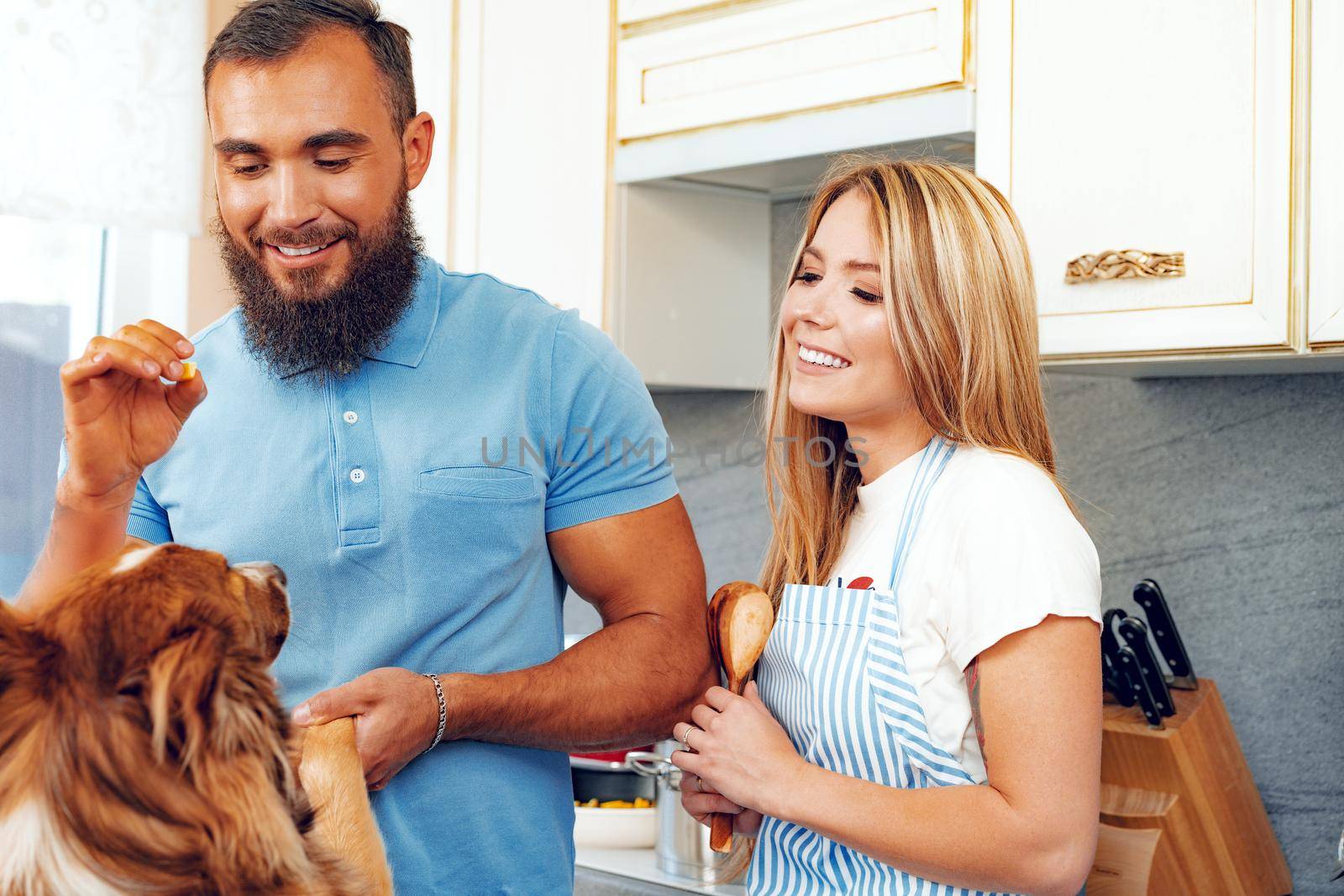 Happy smiling couple cooking food at kitchen with their dog