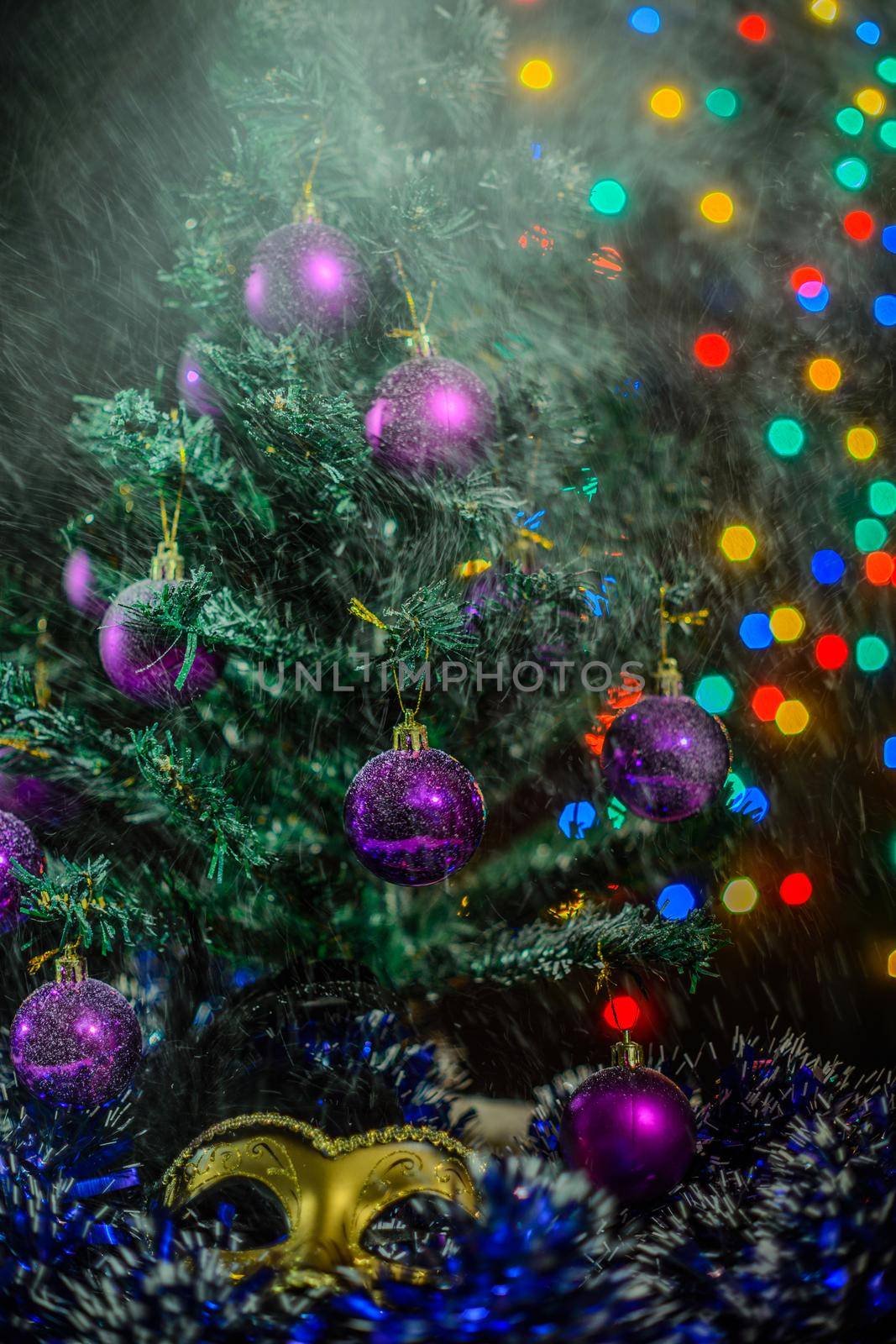 New year theme: Christmas tree white and silver decorations, blue balls, snow, snowflakes, serpentine and golden mask on white retro stylized wood background with yellow backlight