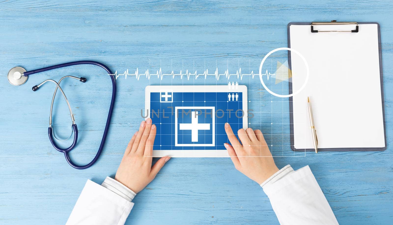 Top view of doctor hands with tablet computer. Therapist in white coat sitting at blue wooden desk. Examination and consultation in clinic. Medical application and online healthcare services.