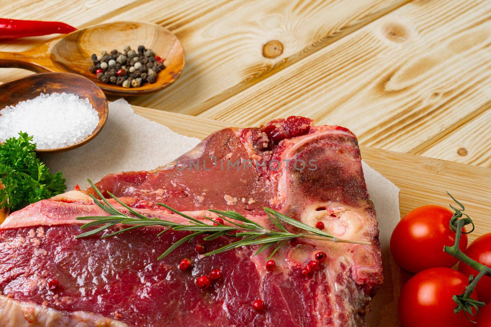Raw t-bone meat with fresh vegetables and rosemary on the table, close up.