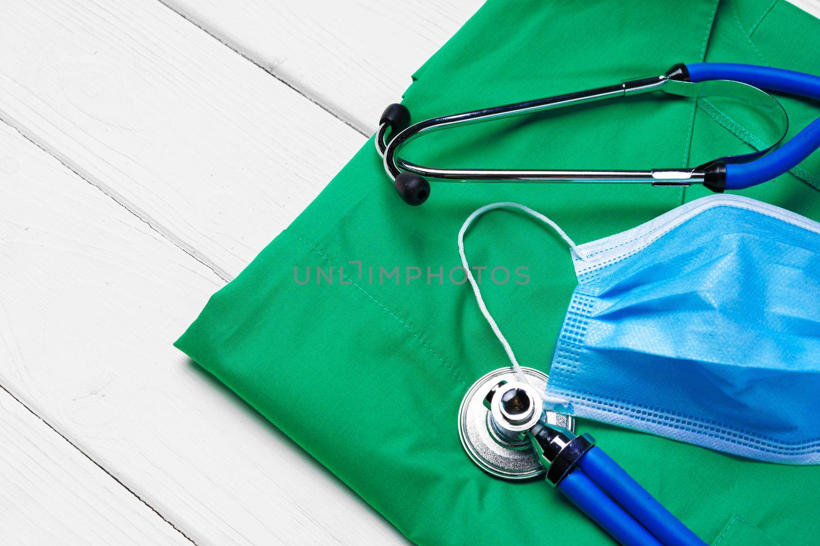 Doctor medical uniform with stethoscope and face mask on white wooden background close up