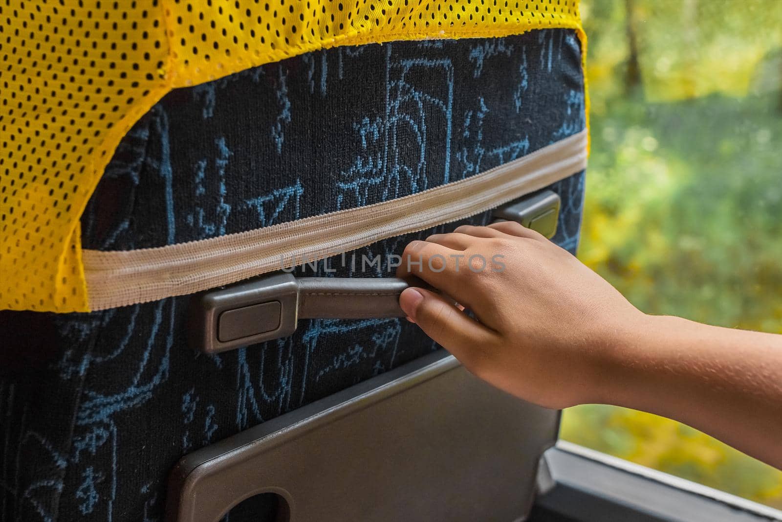 The girl's hand is holding on to the rubber handle of the seat on the bus, close-up.