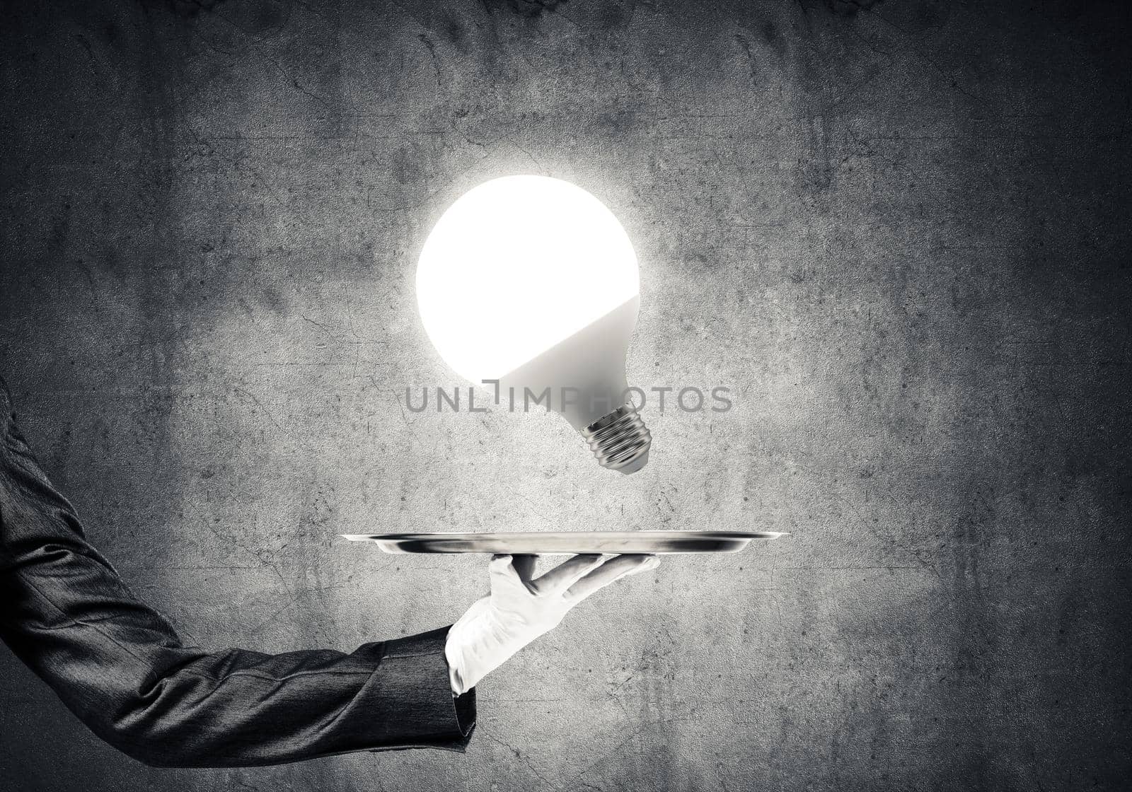 Cropped image of waitress's hand in white glove presenting glowing lightbulb on metal tray