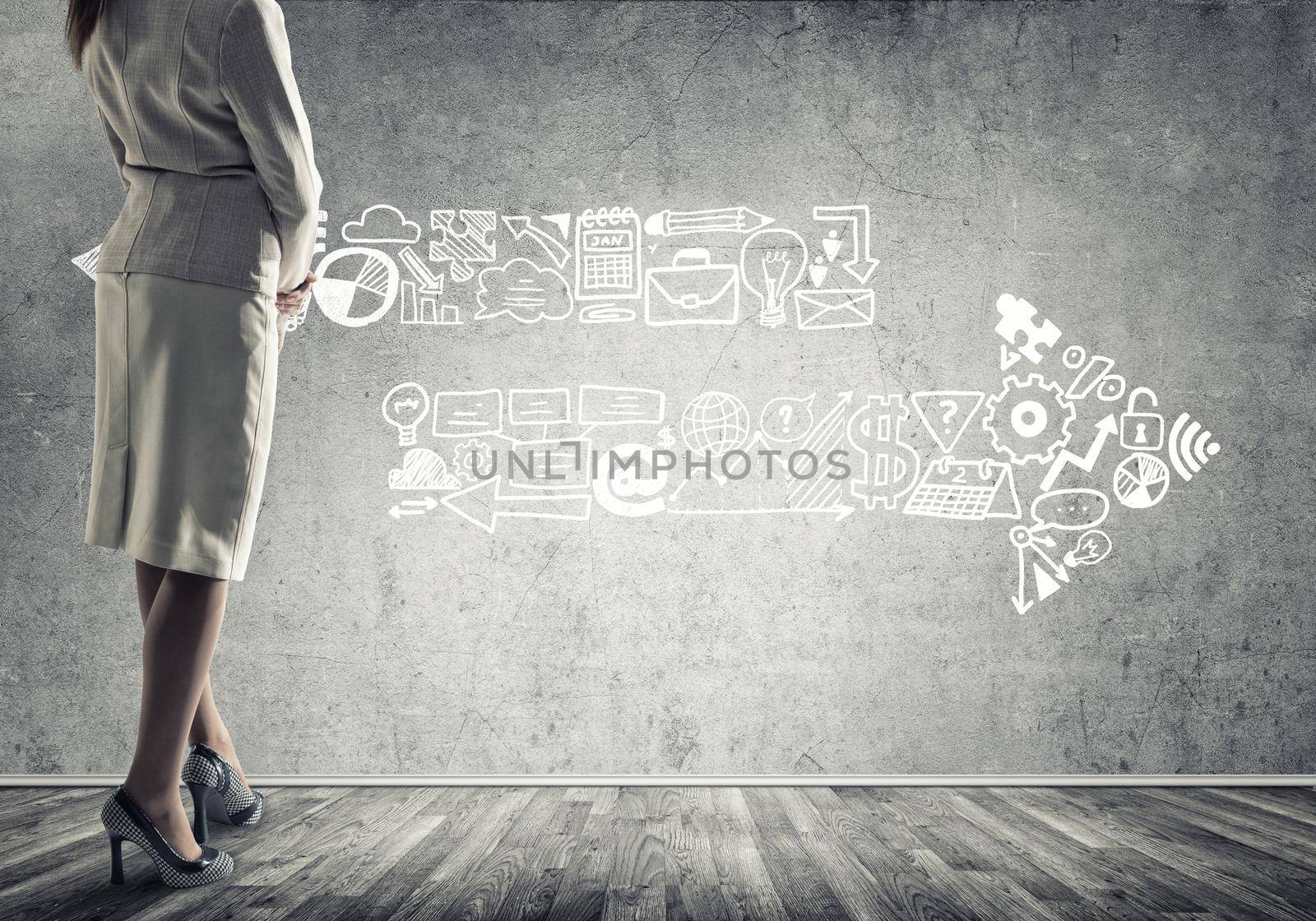 Back view of confident businesswoman in empty concrete room with sketches on wall