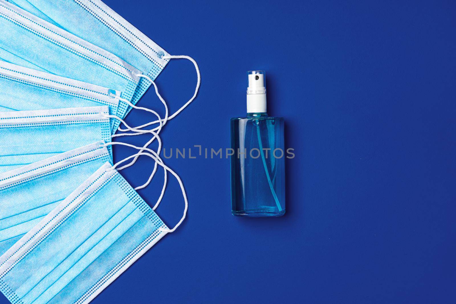 Pile of medical face masks with hand sanitizer on blue background close up