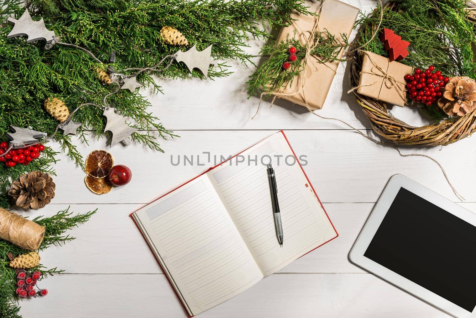 Tablet computer in the human hands. Near the table with tablet computer gift box, christmas bell and fluffy fir branches. Free space for text. top view. Copy space. Closeup