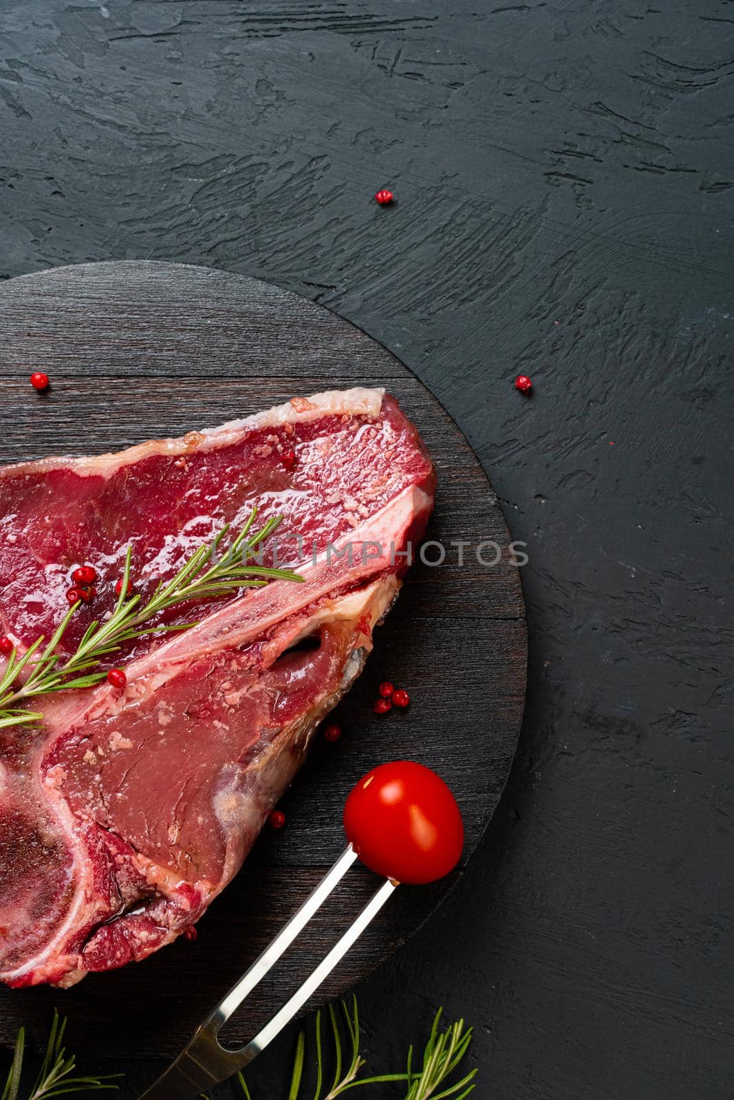 Raw t-bone steak with rosemary, pepper. Prepared for cooking. Close up.