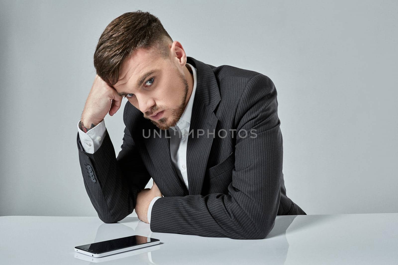 Portrait of attractive young caucasian man using cellular phone while sitting at office table. emotions