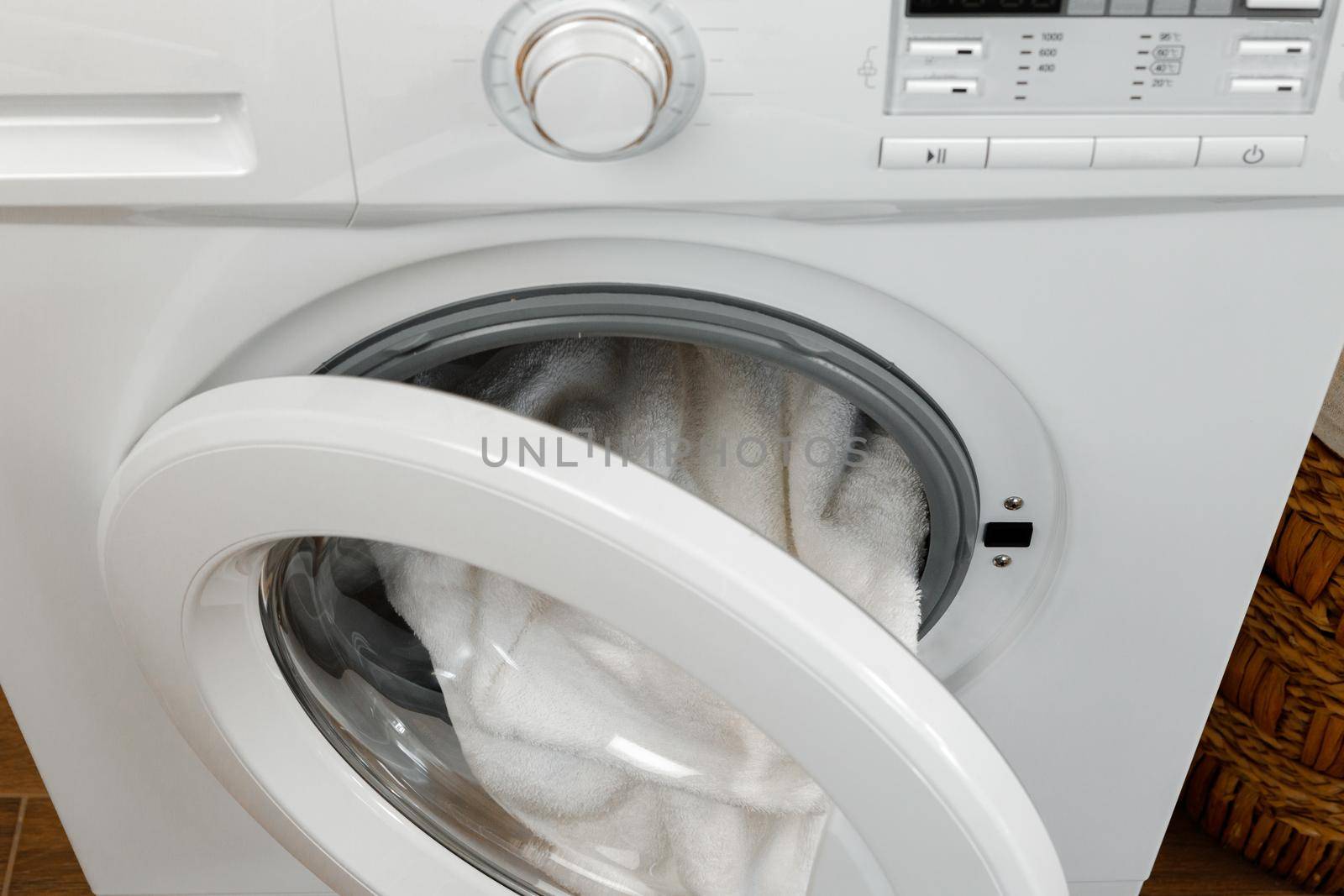 Washing machine with laundry on blue wall background, close up.