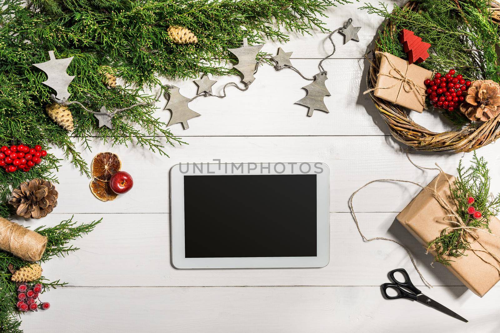 Juniper branches with a Christmas decor. Christmas, New Year background. Coniferous branches of juniper and white tablet with black screen. Top view, flat design. Christmas tree on white wooden background.