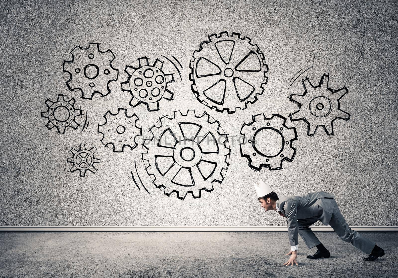 Young handsome businessman wearing white paper crown running and gear mechanism on wall