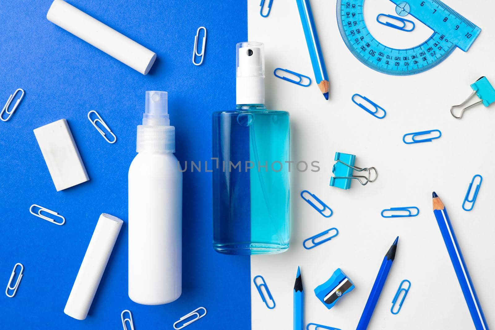 Hand sanitizer and school supplies such as chalks, paper clips on blue and white paper background top view