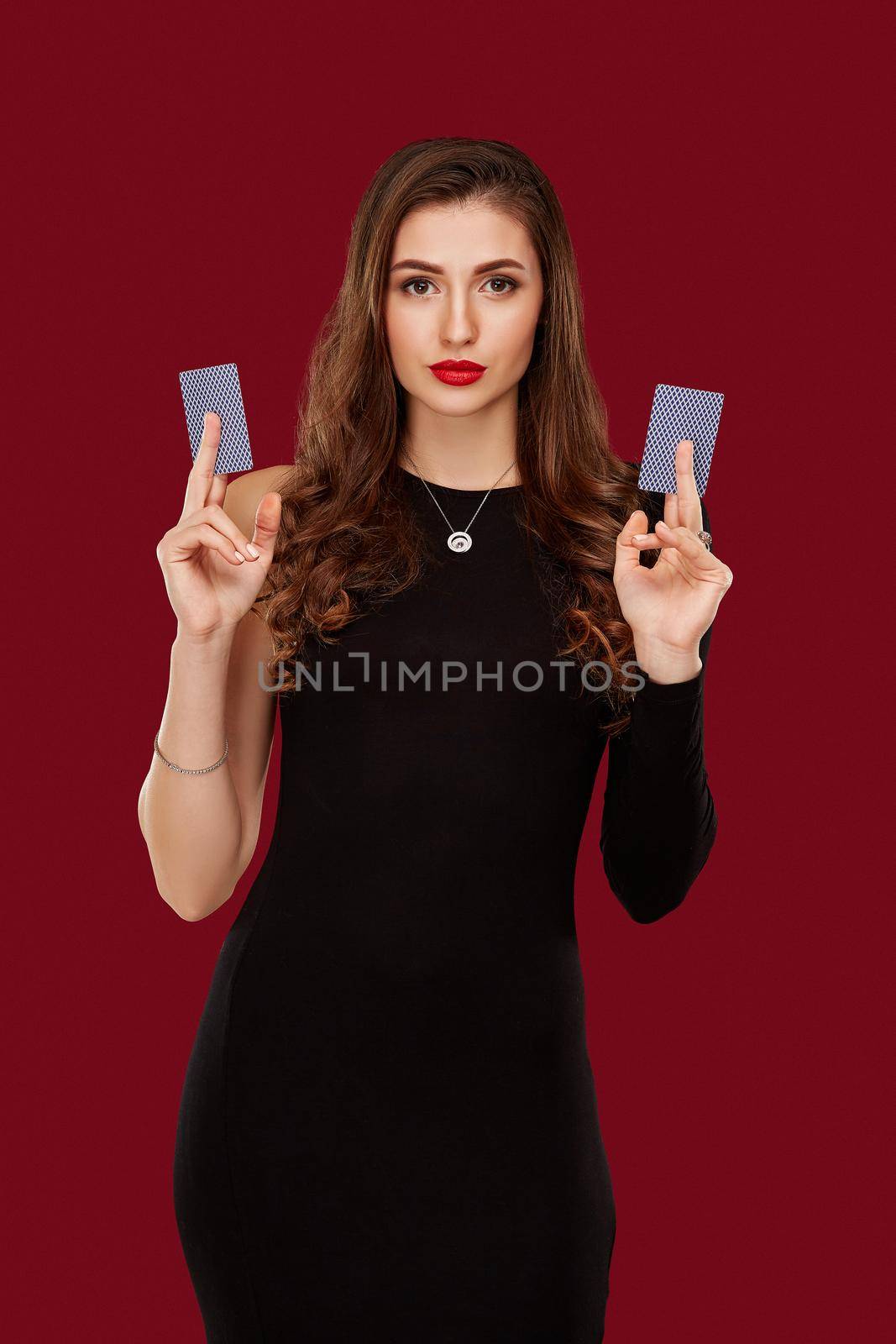 Beautiful caucasian woman in black dress with poker cards gambling in casino. Studio shot on red background. Poker. Two cards in hands