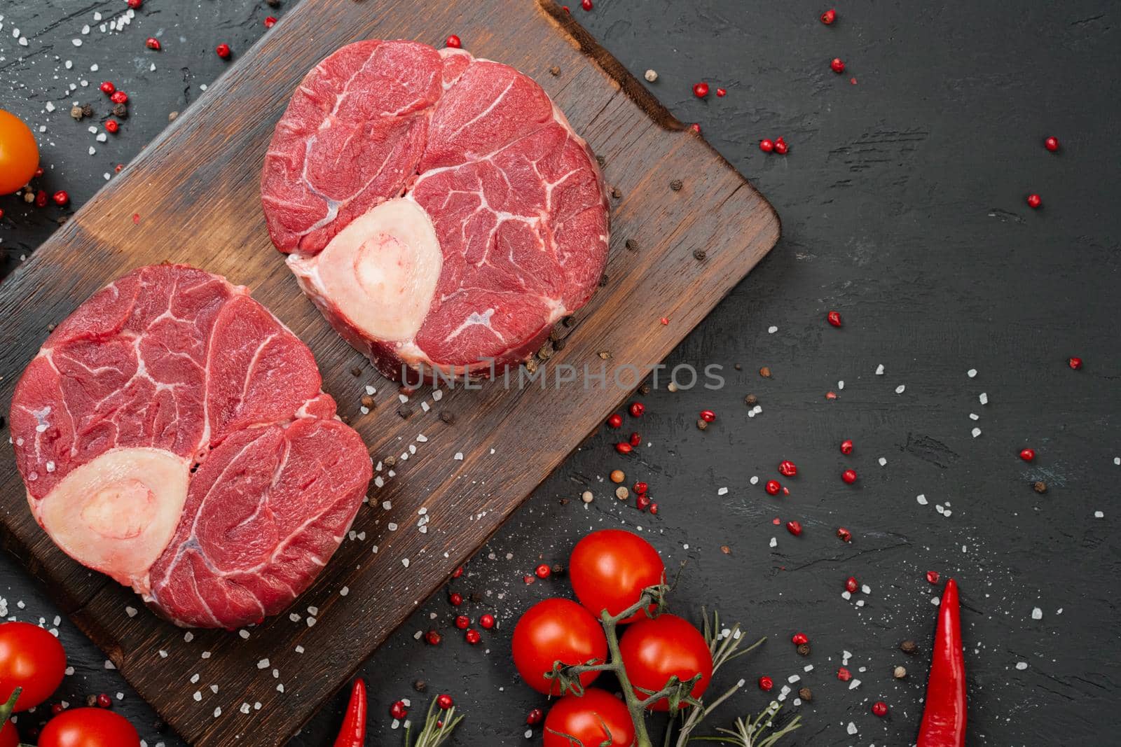 Two raw fresh marbled meat steak on dark background, cherry tomatoes and spices. Close up.