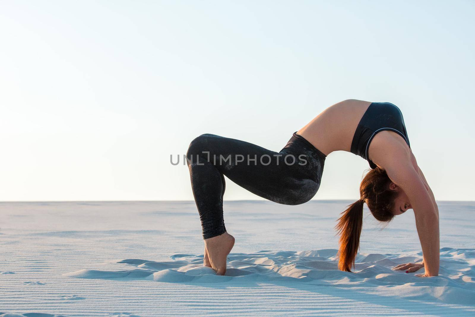 Fitness yoga woman stretching on sand. Fit female athlete doing yoga pose before running training outside in amazing landscape.