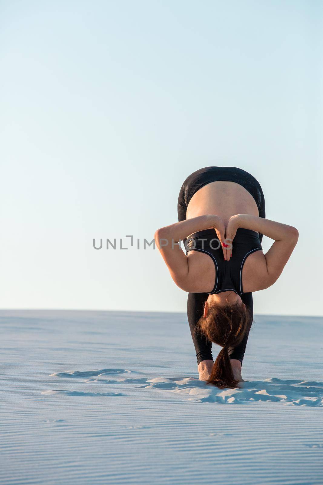 Fitness yoga woman stretching on sand. Fit female athlete doing yoga pose before running training outside in amazing landscape.