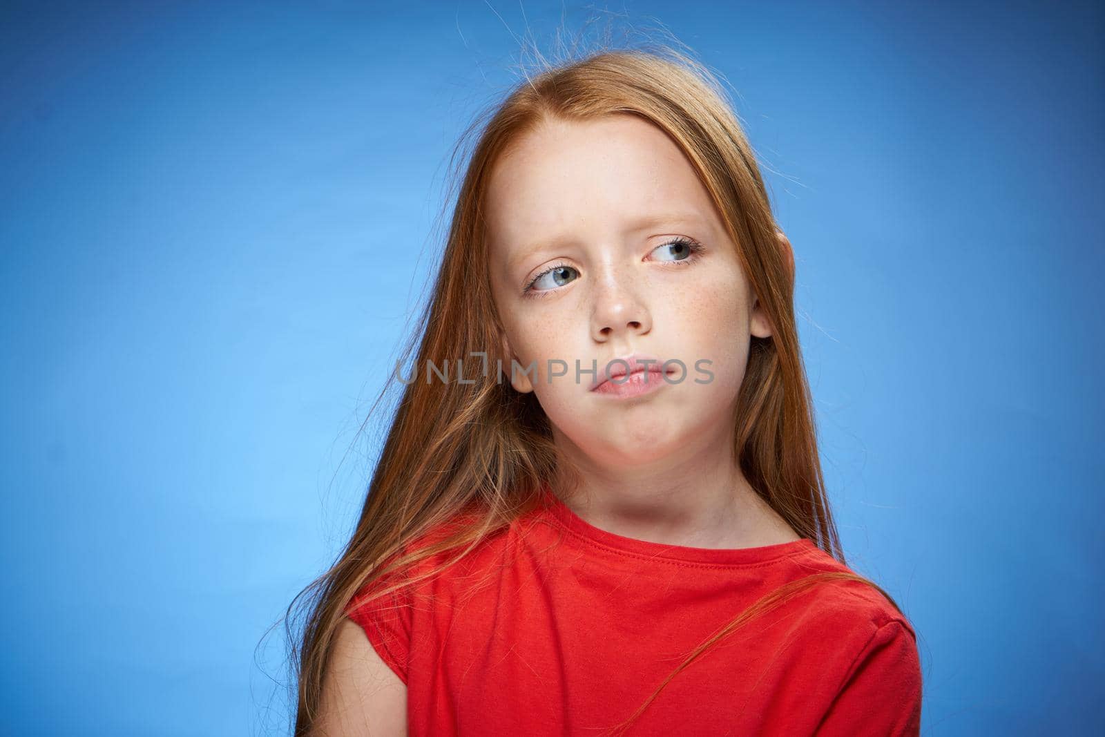 cute red-haired girl in red t-shirt emotions blue background. High quality photo