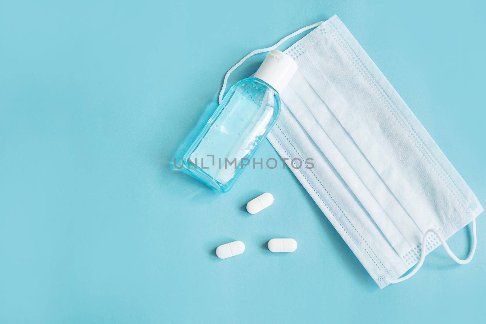 Respiratory mask, atibacterial hand treatment and medicine in capsules on blue background.Virus prevention and treatment.
