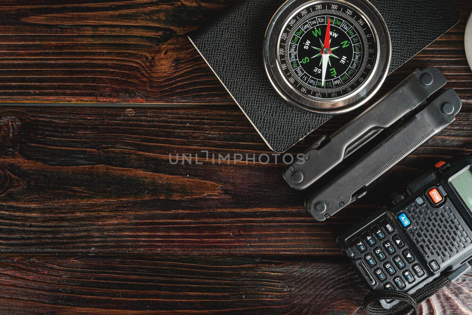 Compass surrounded by mountain gear tools on wooden background, closeup