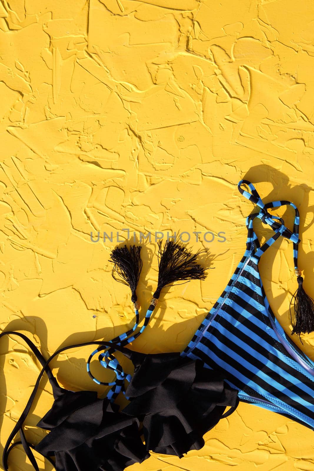 Blue with black stripes female swimsuit and sunglasses on a yellow background. The concept of a beach holiday, a trip to the sea, accessories for swimming, UV protection, tanning. Copyspace. Flatlay by Simol