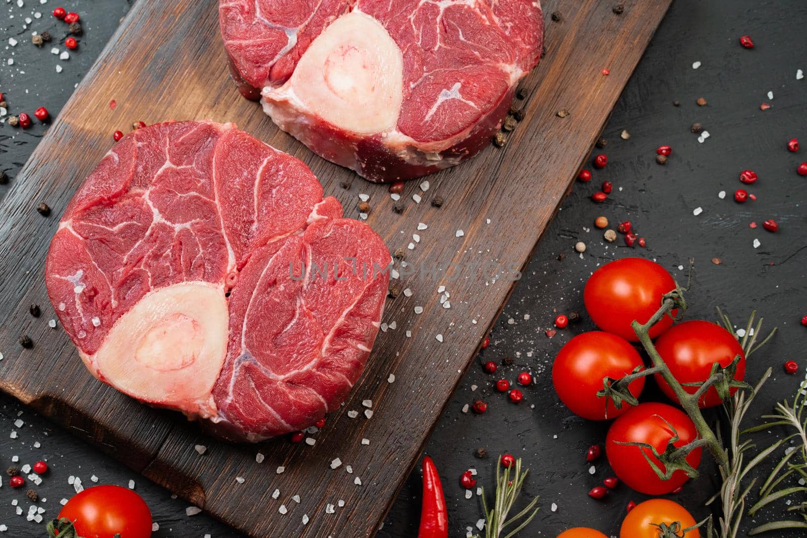 Two raw fresh marbled meat steak on dark background, cherry tomatoes and spices. Close up.