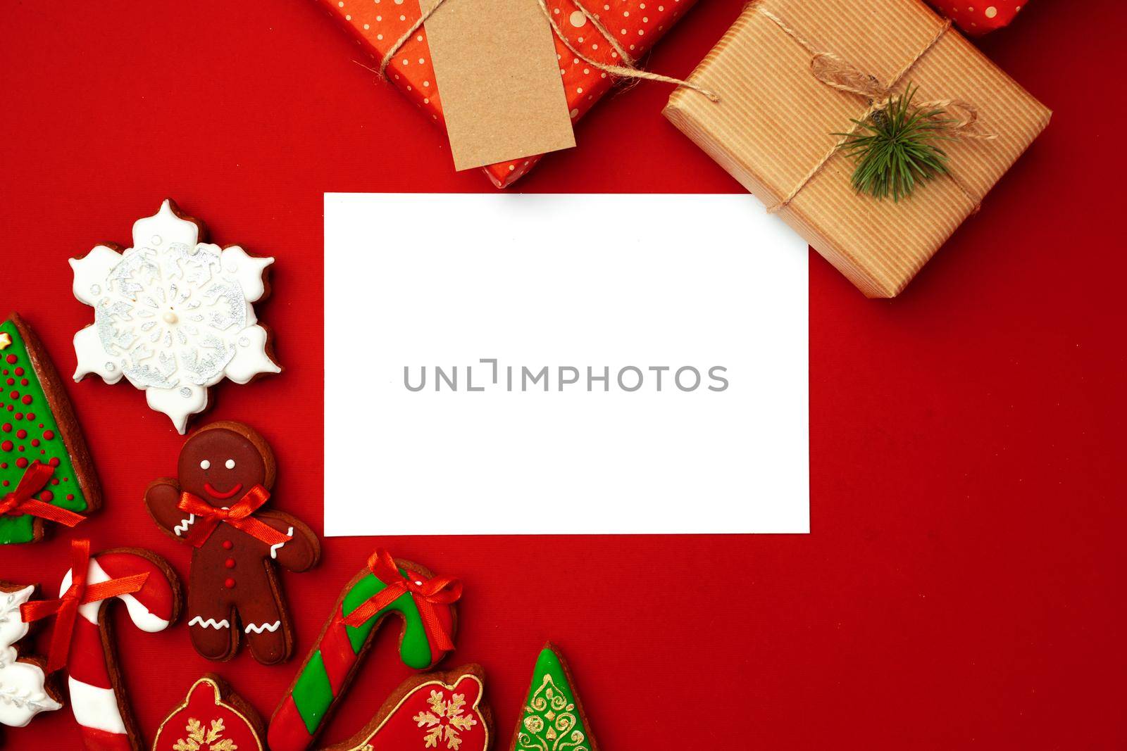 Blank sheet of paper with Christmas gift and gingerbread cookies on red background flat lay