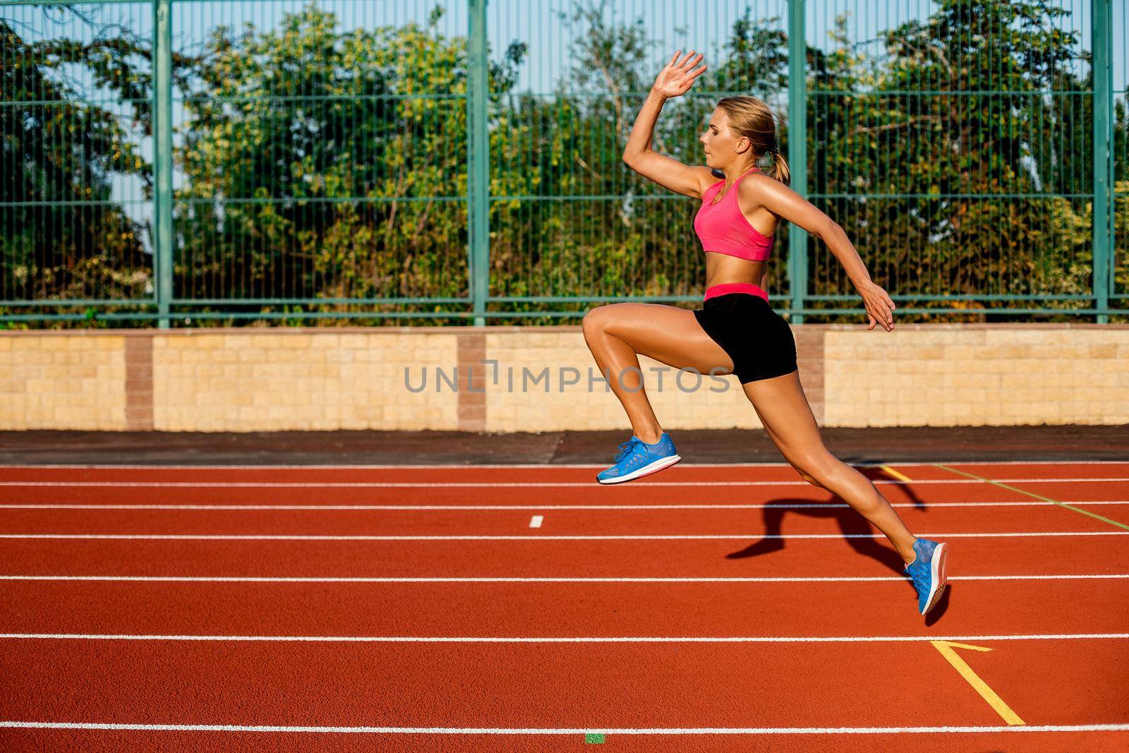 Side view beautiful young woman exercise jogging and running on athletic track on stadium. Sport, healthy lifestyle concept.