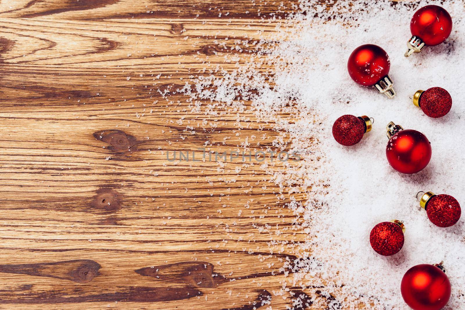 Wooden board with snow and red Christmas baubles top view
