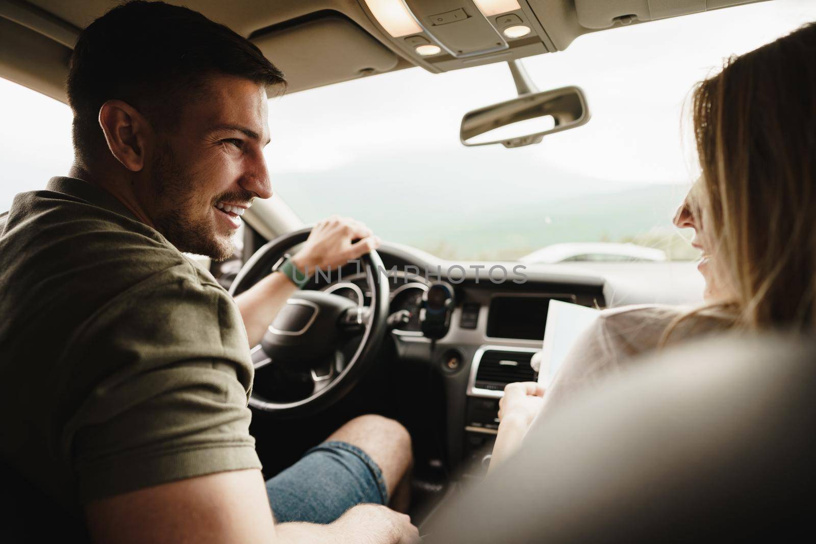 Beautiful young smiling couple sitting on front passenger seats and driving a car