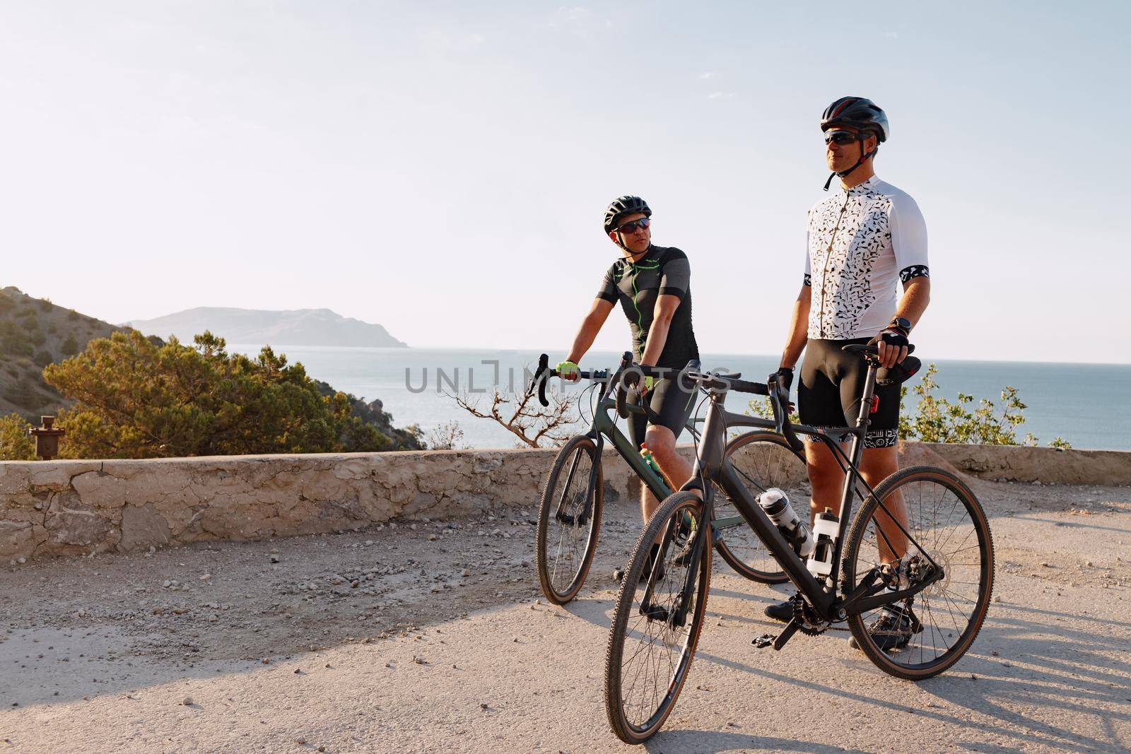 Two male cyclists stand on the coastal road and have a rest
