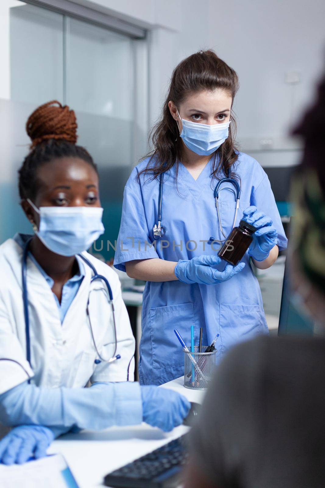 Medical team discussing with african american sick patient explaining medication treatment during clinical appointment in hospital office. Women wearing protective face mask against covid19