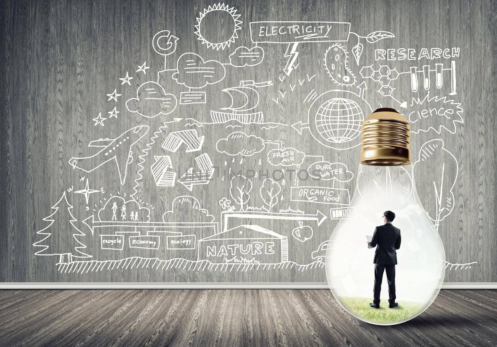 Businessman inside of light bulb in empty concrete room and sketches on wall
