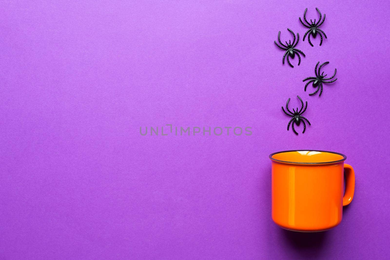 Orange mug on a purple background with spiders. The concept of the Halloween holiday. Terrible scenery, terrible drink, fun. Copy space, mock up, flatly
